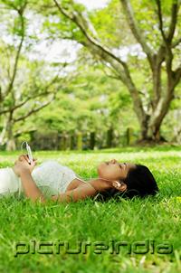 PictureIndia - Young woman lying on grass, listening to music with headphones