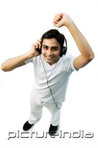 PictureIndia - Young man listening to headphones, arm raised, smiling at camera