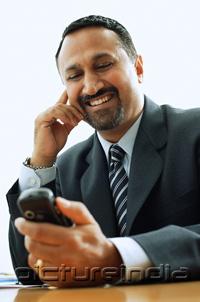 PictureIndia - Businessman looking at PDA phone, smiling