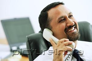PictureIndia - Businessman using telephone, looking away
