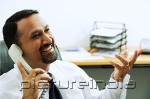 PictureIndia - Businessman using telephone, looking away, hand raised