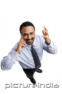 PictureIndia - Businessman using mobile phone, looking at camera, hand raised