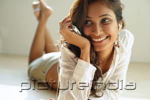 PictureIndia - Woman listening to music from MP3 player, lying on front, smiling