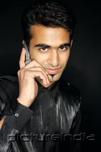 PictureIndia - Man using mobile phone, looking at camera