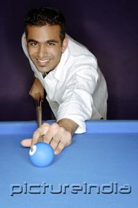 PictureIndia - Young man playing pool, smiling at camera, portrait