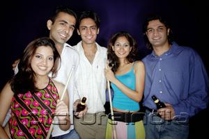 PictureIndia - Young adults standing together, holding pool cue and beer bottles, smiling at camera