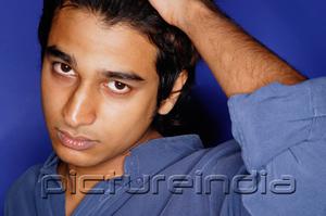 PictureIndia - Man in blue shirt against blue background, hand on head