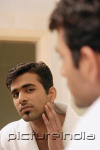 PictureIndia - Man wearing bathrobe, looking in mirror, touching his face