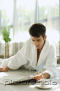 PictureIndia - Man in bathrobe, lying on floor, reading newspaper