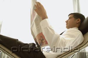 PictureIndia - Businessman reclining on chair, reading newspaper