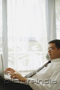 PictureIndia - Businessman reclining on chair, using laptop