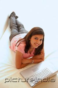 PictureIndia - Woman at home, lying on bed, arms crossed, laptop open in front of her