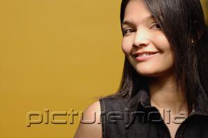 PictureIndia - Young woman against yellow background, looking at camera, portrait