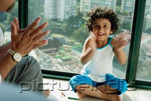 PictureIndia - Girl sitting on floor, clapping hands, smiling at camera, father next to her