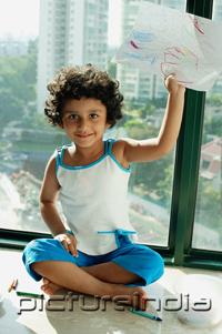 PictureIndia - Girl sitting on floor holding up drawings, smiling at camera