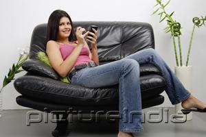 PictureIndia - Woman sitting on armchair using PDA, smiling at camera