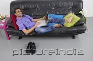 PictureIndia - Man sitting on sofa with laptop, smiling at camera
