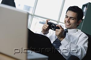 PictureIndia - Young businessman playing with Playstation Portable