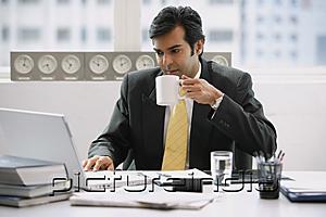 PictureIndia - Businessman in office using laptop, drinking from cup