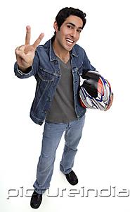 PictureIndia - Man carrying motorcycle helmet, looking up at camera, making hand sign