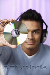 PictureIndia - young man with headphones on, holding compact disc in front of him