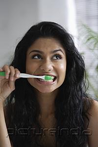 PictureIndia - Head shot of Indian woman brushing her teeth and looking up