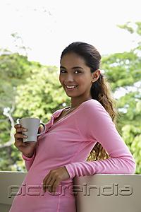 PictureIndia - Young woman holding mug leaning on balcony