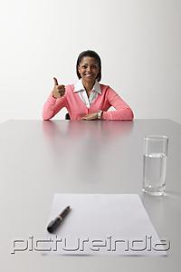 PictureIndia - Young woman sitting at table during interview giving thumbs up sign