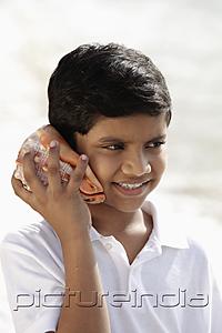 PictureIndia - young boy listening to sea shell and smiling