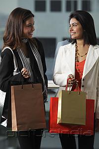 PictureIndia - two woman holding shopping bags and looking at each other smiling.