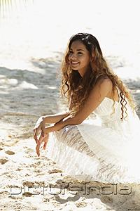 PictureIndia - young woman sitting on sand at the beach smiling