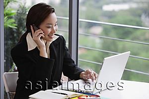 Asia Images Group - businesswoman at laptop with cell phone