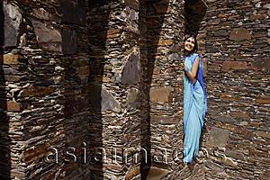 Asia Images Group - young woman in sari, peeking from behind brick pillar