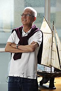 AsiaPix - mature man folding his arms and smiling in front of model sail boat