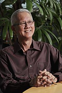 AsiaPix - mature man sitting in front of plant smiling