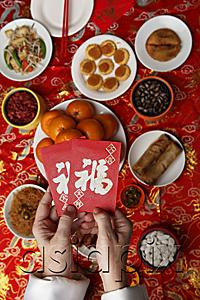 AsiaPix - Hands holding red envelopes (Hong Bao) over table with Chinese food.