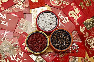 AsiaPix - Different red envelopes scattered on table with melon seeds in bowls.