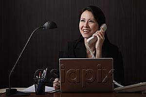 AsiaPix - Chinese woman sitting at desk talking on phone and smiling
