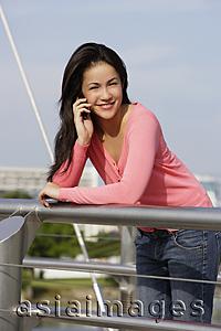 Asia Images Group - Young woman leaning over bridge on cell phone
