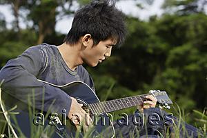 Asia Images Group - Young man playing guitar in grass