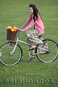 Asia Images Group - Young woman riding bike with basket full of flowers