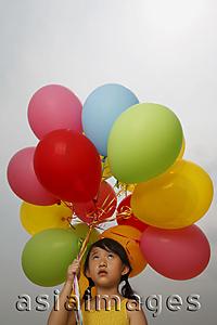 Asia Images Group - Young girl holding balloons looking up.