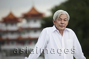 Asia Images Group - Older man standing outside in front of pagodas