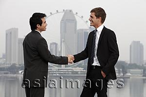 Asia Images Group - Chinese and Caucasian man shaking hands in front of skyline