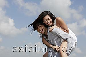 Asia Images Group - young man carrying a woman on his back laughing, blue sky with clouds as background