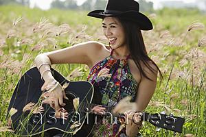 Asia Images Group - Happy woman playing guitar in grassy field