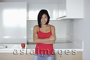 Asia Images Group - young woman standing in kitchen with an apple, wearing red top