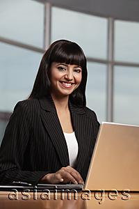Asia Images Group - Indian woman smiling and working on laptop