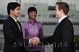 Asia Images Group - Indian and Caucasian man shaking hands while woman looks on.