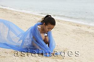 Asia Images Group - Young girl with blue cloth wrapped around her sitting on sand.